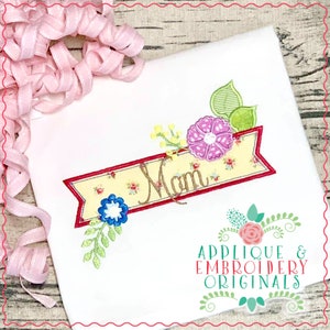 Puede incluir: Una pancarta amarilla con un borde rojo y un patrón floral. La pancarta dice "Mamá" en letras cursivas marrones. La pancarta está decorada con hojas verdes, flores rosas y flores azules. La imagen incluye el texto "Applique & Embroidery Originals".