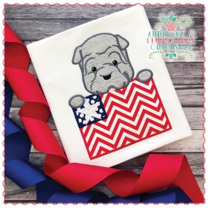 Puede incluir: Un bulldog gris sosteniendo una bandera estadounidense roja, blanca y azul con estrellas blancas. El bulldog asoma por detrás de un patrón de chevron rojo y blanco.