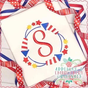 Puede incluir: Diseño bordado en rojo, blanco y azul de una letra S rodeada de fuegos artificiales y estrellas. El diseño está sobre un fondo de tela blanca. Applique & Embroidery Originals.