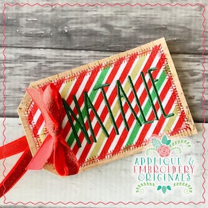 May include: A red, green and gold striped fabric gift tag with the name "Natalie" embroidered in green thread. The tag is tied with a red ribbon bow and has a cork backing. The tag is labelled "Applique & Embroidery Originals".