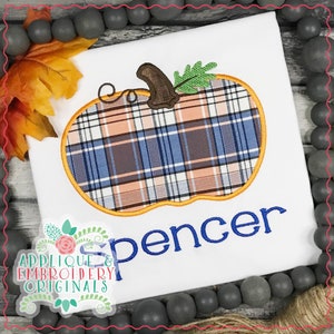 May include: White t-shirt with an embroidered plaid pumpkin and the name "Spencer" in blue thread. The pumpkin has a brown stem and a green leaf.
