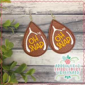 May include: A pair of brown leather earrings with a white wishbone design and the text "Oh Snap" in yellow embroidery.