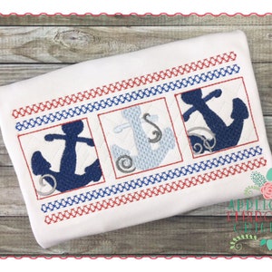 May include: Three embroidered anchors in blue, light blue, and white, with a red and blue border. The anchors are in a row, each in a square frame. The background is a white fabric.