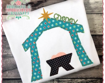 May include: A white t-shirt with a teal blue and red polka dot manger scene with a gold star and the name "Cheney" embroidered on it.