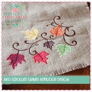 May include: Embroidered applique design featuring a vine with scrolling leaves in shades of red, orange, yellow, green, and brown. The design is stitched on a beige burlap fabric. The text "AEO SCROLLED LEAVES APPLIQUE DESIGN" is displayed below the design.