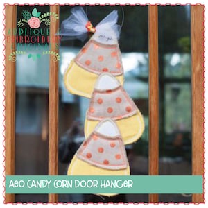May include: Three felt candy corn door hangers in yellow, orange, and white with brown polka dots. The door hangers are hanging on a wooden door.