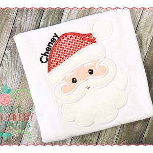 May include: White personalized t-shirt with a red and white embroidered Santa Claus face. The name "Cheney" is embroidered above the Santa Claus face.