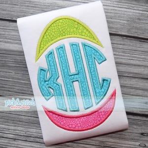 Puede incluir: Tela blanca con un diseño de monograma turquesa, con las letras KHC, dentro de una forma de huevo estilizada. El diseño incluye una parte superior verde y una inferior rosa, con el texto "pick & stitch applique designs" en la parte inferior.