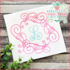 May include: Pink and blue embroidery design featuring a decorative swirl frame with a letter L in the center. The design is on a white fabric background. Applique & Embroidery Originals.