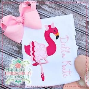 Può includere: Una maglietta bianca con un fenicottero rosa che indossa un tutù rosa e scarpette da ballet rosa. Il fenicottero è ricamato sulla maglietta. Il nome "Della Kate" è ricamato sulla maglietta in corsivo.