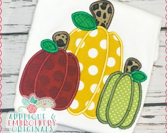 May include: Three embroidered pumpkins in different colors and patterns. The pumpkins are red with white polka dots, yellow with white polka dots, and green with white hearts. The pumpkins are on a white background.