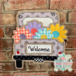 May include: A grey and white pickup truck with a hessian bed filled with colourful flowers. The truck has a sign that says "Welcome".