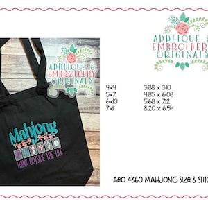 K&ouml;nnte beinhalten: Schwarze Tragetasche mit dem Wort "Mahjong" in T&uuml;rkis und rosa floralen Akzenten. Der Satz "Think Outside The Tile" befindet sich unter dem Mahjong-Design. Die Tasche zeigt auch das Logo "Applique & Embroidery Originals".