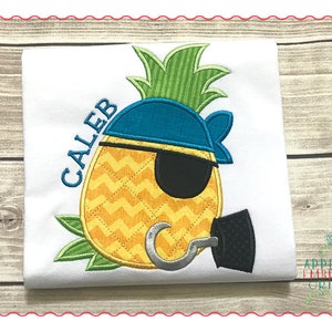 May include: Embroidered design of a pineapple wearing a blue pirate hat and eyepatch, holding a hook. The name "Caleb" is embroidered above the pineapple.