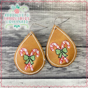May include: A pair of brown teardrop-shaped earrings with a white stitched border. Each earring features an embroidered design of two candy canes with a green bow.