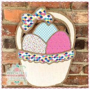 May include: A burlap Easter basket with a colorful bow and three decorated eggs. The eggs are pink with white polka dots, blue with white polka dots, and multi-colored with white polka dots. The basket is decorated with a colorful scale pattern.