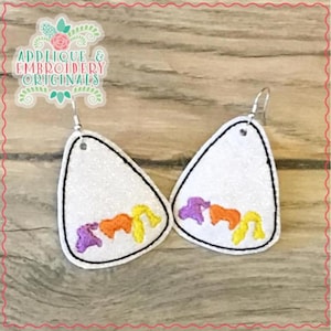 May include: A pair of white, teardrop-shaped earrings with a glittery texture. Each earring features embroidered purple, orange, and yellow shapes, outlined in black. The earrings have silver-colored fish hook closures. The image also includes the text "Applique & Embroidery Originals".
