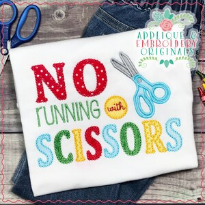 Op de afbeelding: Wit T-shirt met de tekst "NO RUNNING with SCISSORS" in kleurrijke geborduurde letters. Het woord "NO" is rood met witte stippen, "RUNNING" is groen, "with" is geel en "SCISSORS" is een mix van blauw, groen, geel en rood. Een paar blauwe scharen is geborduurd boven de tekst.