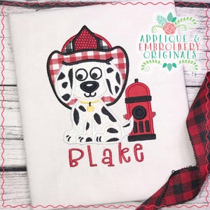 May include: Embroidered design of a Dalmatian dog wearing a red and white checkered firefighter hat, sitting next to a red fire hydrant. The name "Blake" is embroidered below the dog and fire hydrant.
