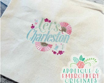May include: Cream tote bag featuring the embroidered phrase "Let's Charleston" in light blue and green, with pink fan and floral motifs. A sticker in the corner reads "Applique & Embroidery Originals".