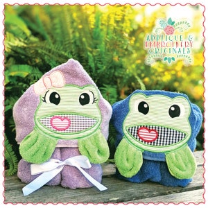 May include: Two hooded towels with frog appliques. One towel is purple with a pink bow and the other is blue. Both frogs have green bodies, black eyes, and a red heart on their mouths.