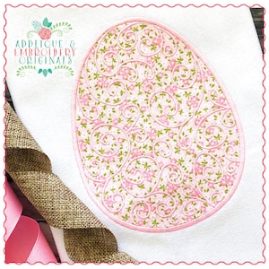 May include: A pink and green embroidered oval design with a floral pattern. The design is on a white fabric background.