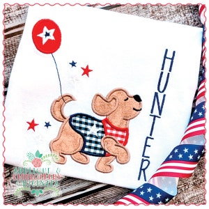 Puede incluir: Una camiseta blanca con un perro marrón y blanco que sostiene un globo rojo con una estrella blanca. El perro lleva un chaleco azul y blanco a cuadros y una camisa roja y blanca a cuadros. El nombre "Hunter" está bordado en azul en el lado derecho de la camiseta.