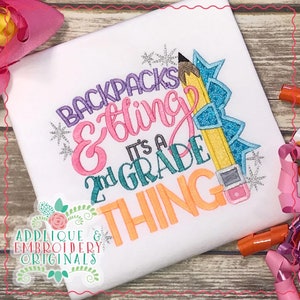 May include: A white t-shirt with an embroidered design that says "Backpacks & bling it's a 2nd grade thing". The design features a large pencil with a blue and silver glitter bow, and a small silver star.