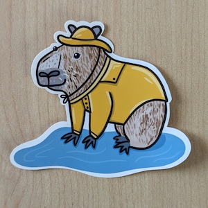 May include: A cartoon capybara wearing a yellow raincoat and a yellow hat, standing in a blue puddle.