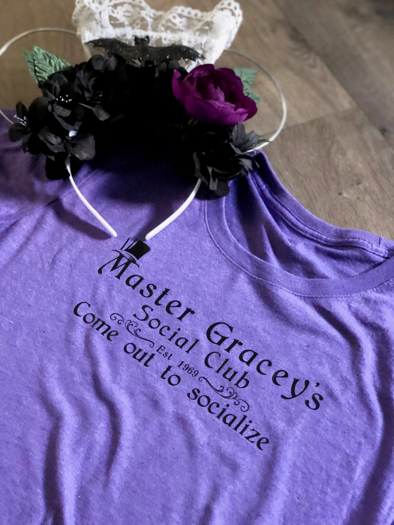 Puede incluir: Camiseta morada con texto negro que dice "Master Gracey's Social Club Est. 1969 Come out to socialize".