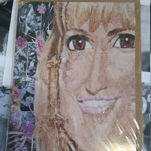 May include: A close-up of a woman's face in a painting. The woman has blonde hair and is smiling. The painting is made with a variety of textures and materials, including paint, fabric, and paper.