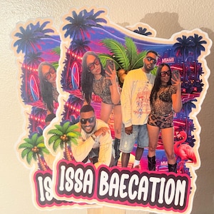 May include: A decorative cake topper featuring a vibrant Miami-themed background with palm trees, neon lights, and a flamingo. The design includes a photo of a couple and the text "IS ISSA BAECATION" in bold white letters on a pink and black background.