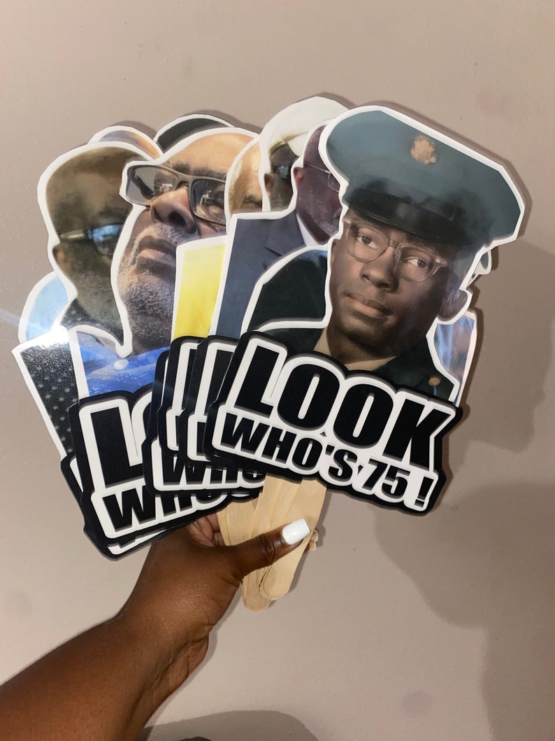 May include: A collection of handheld party props featuring die-cut photographic portraits of a person at different ages. Each cutout is attached to a wooden stick and displays the bold black and white text LOOK WHO'S 75! at the bottom edge.