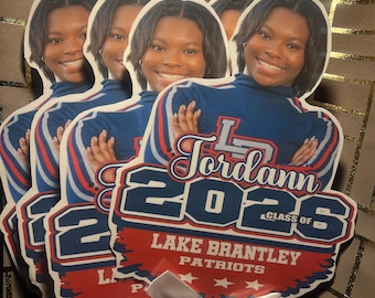 May include: A custom graduation fan featuring a portrait of a smiling person wearing a blue shirt. The design includes the name Jordann, the year 2026, the text Class of, Lake Brantley, and Patriots, accented with a white satin ribbon at the base.
