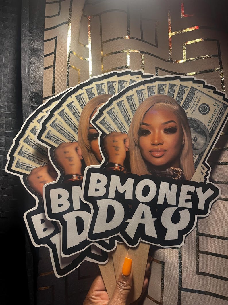 May include: A fan-shaped cutout featuring a portrait of a person with blonde hair, layered over a background of one hundred dollar bills. The text BMONEY DAY is printed in bold white letters with a black outline at the bottom of the cutout.