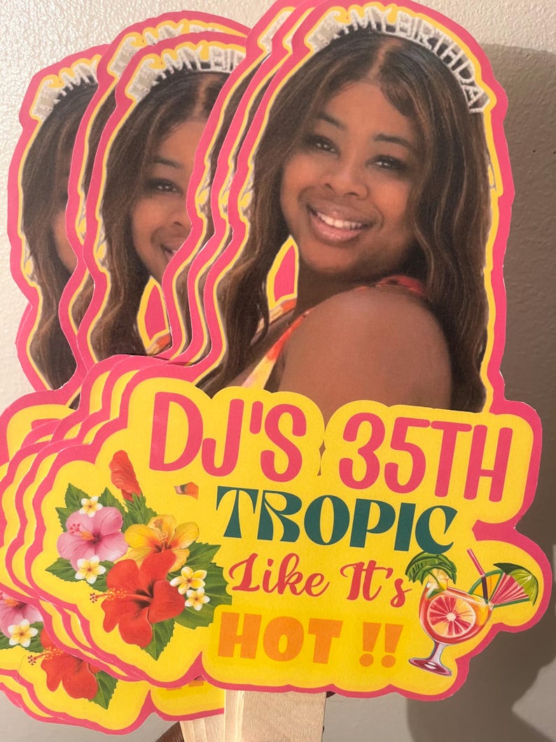 May include: A custom die-cut party sign featuring a photograph of a smiling person wearing an IT'S MY BIRTHDAY headband. The yellow sign displays the text DJ'S 35TH TROPIC LIKE IT'S HOT!!, decorated with colorful hibiscus flowers and a tropical cocktail.
