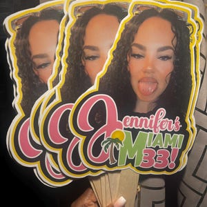 May include: Three identical custom die-cut paper fans featuring a photographic portrait of a person with curly dark hair sticking their tongue out. The text reads Jennifer's MIAMI 33! in pink and green, accompanied by a small palm tree graphic.