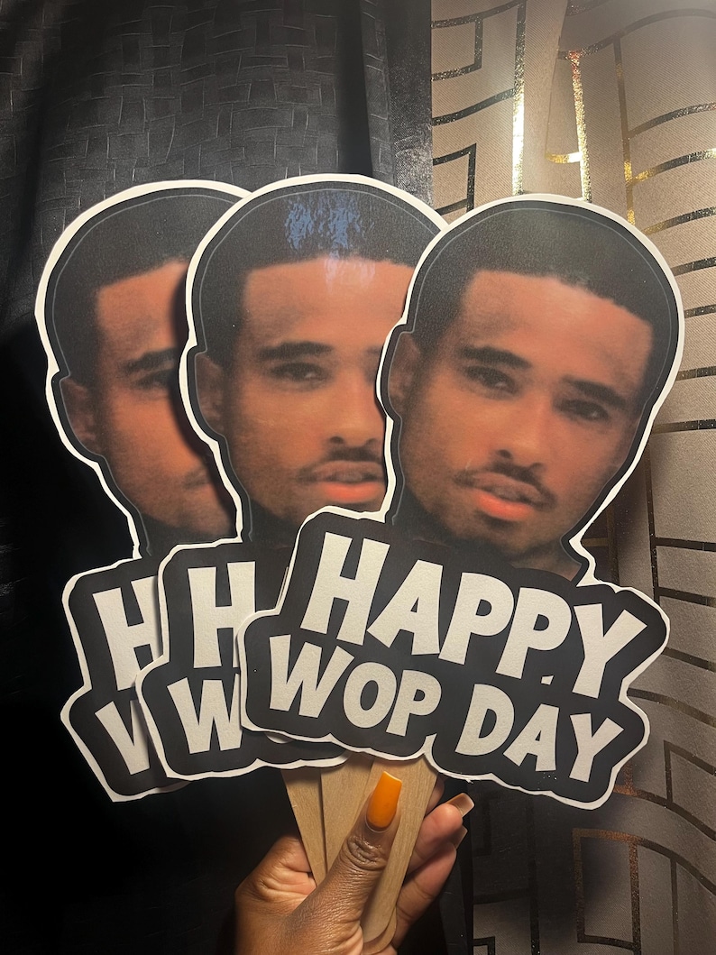 May include: Three identical handheld paper cutouts featuring a photographic portrait of a man with a mustache and goatee. Below the portrait, bold white text on a black background reads "HAPPY WOP DAY" in a sans-serif font. Each cutout has a wooden stick.