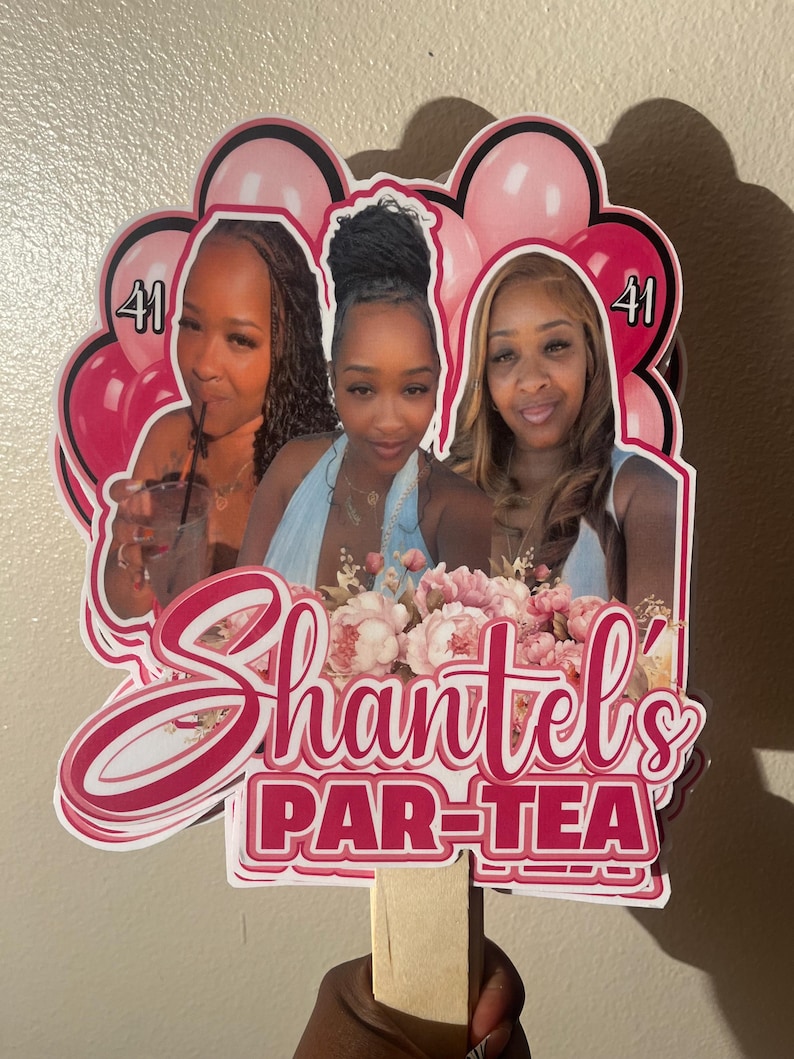 May include: A custom cake topper featuring three photographs of the same person, surrounded by pink balloons and floral accents. The text reads 'Shantel's PAR-TEA' with the number '41' displayed on both sides. The topper is attached to a wooden stick.