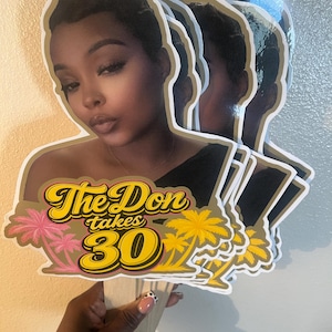 May include: A stack of custom die-cut cardstock cake toppers featuring a photographic portrait of a person with short dark hair. The design includes the yellow and black text The Don takes 30, accented by pink and yellow palm tree illustrations.