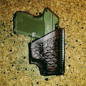 Könnte beinhalten: Eine grüne Pistole mit einem schwarzen Lederholster. Das Holster hat ein dekoratives Muster.