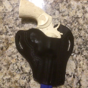 May include: A black leather holster with a white revolver inside.