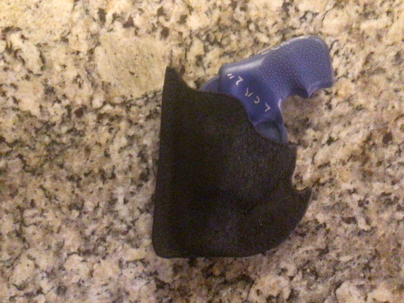 May include: A black holster with a blue object inside. The holster is made of a textured material. The blue object has the text "< CR 2" on it.