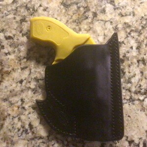 May include: A yellow handgun in a black leather holster. The holster has a stitched edge and a decorative design.