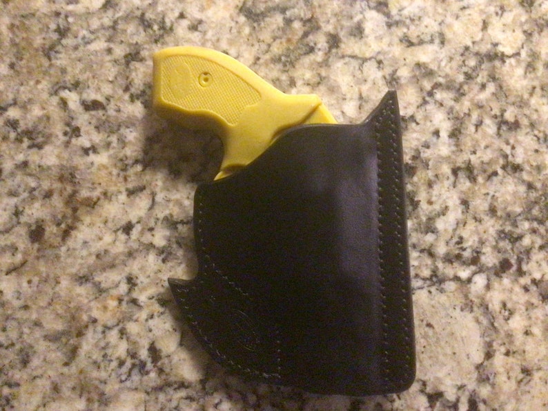 May include: A yellow handgun in a black leather holster. The holster has a stitched edge and a decorative design.