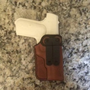 Puede incluir: Una funda de cuero marrón con una pistola blanca en su interior. La funda tiene un clip para el cinturón y una solapa que cubre la protección del gatillo.