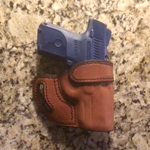 May include: A blue handgun in a brown leather holster. The holster has a strap and stitching detail.