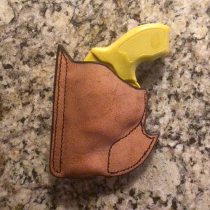 May include: A yellow handgun in a brown leather holster. The holster has a stitched design.