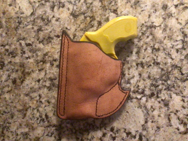 May include: A yellow handgun in a brown leather holster. The holster has a stitched design.
