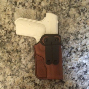 May include: A brown leather holster with a black clip and a white plastic gun inside.